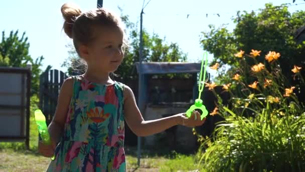 Little girl playing in the village in summer day with soap bubbles. — Stock Video