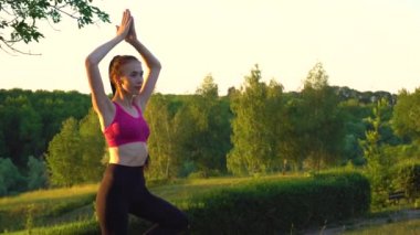 Kadın balıkçıl pozisyonunda duruyor ve meditasyon yaparken ileriye bakıyor..