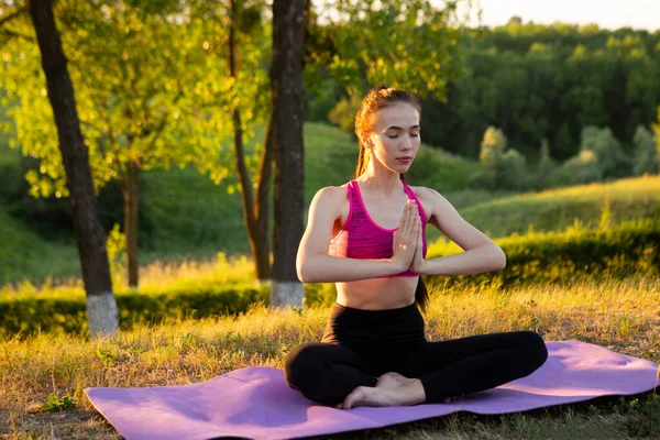 Donna senza scarpe è seduto su un tappeto e pratica yoga. — Foto Stock