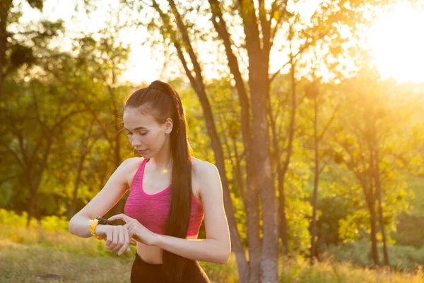 Frau überprüft tragbares Gerät für Fitness und Gesundheitsverfolgung im Park. — Stockfoto