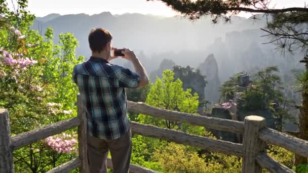 Turista vytvářet snapshoty rozhledů vertikální útesy v destinaci Wulingyuan s jeho smartphone během za jasného slunečného dne. Zhangjiajie, Čína. UHD — Stock video