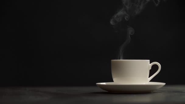 Steaming coffee cup on black background. Puffs of steam slowly coming from a white cup of hottest coffee. Slow motion shot — Stock Video