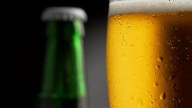 Altın köpüklü bira cam dönen waterdrops ile kaplı. Yeşil bira şişesi içinde belgili tanımlık geçmiş. Atış, 4 k yakın çekim