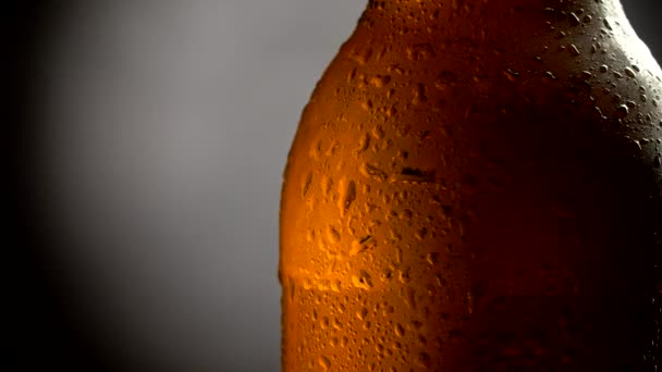 Бутылка пива, покрытая водопадами на сером и черном фоне. Крупный план, 4К — стоковое видео
