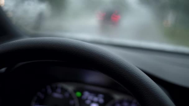 Coche bajo fuerte lluvia con pandilla de emergencia encendida. Vista desde el parabrisas al semáforo bajo la lluvia. UHD 4K — Vídeo de stock