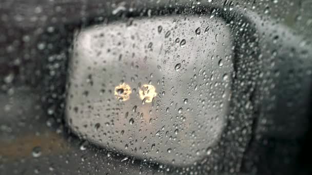 Regndroppar på bilrutan och spegel under regn. Oskärpa trafikljus på spegeln — Stockvideo