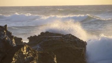 Yavaş yavaş gün batımı ışınları bir kayalık kıyıları karşı kırma okyanus dalgaları öfkeli köpüklü sörf. Yavaş hareket görünümü
