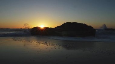 Islak kum manzara plaj ve bu sel bir Atlantik Okyanusu dalga. Güneş siyah kaya günbatımı sırasında Portekiz'de kayar. UHD
