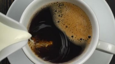 Lezzetli beyaz süt yavaşça kahverengi lezzetli köpüklü kahve bir bardak içine bir sürahi dökme. Üstten aşağı yavaş hareket çekimi