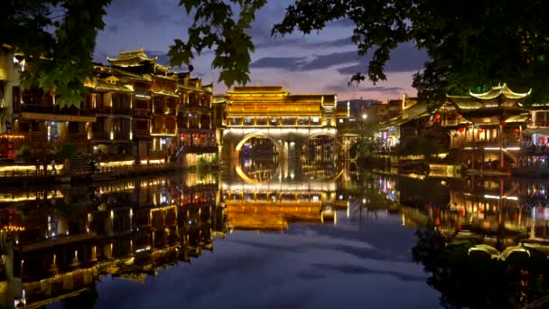 Condado de Fenghuang, China. Vista nocturna de las luces de Fenghuang Ancient Town. Hermosos reflejos de luces de colores se ven en el río Tuojiang. Fenghuang significa Fénix en chino. 4K — Vídeo de stock