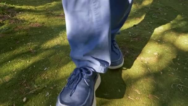 Man draagt blauwe broek en blauwe loafer schoenen, wandelen op groene mos door de zon en schaduwen. UHD — Stockvideo