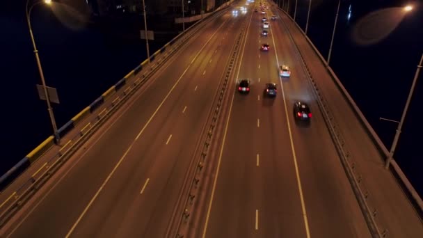 Voando sobre o tráfego do carro da noite em uma ponte sobre um rio. Tiro aéreo, UHD — Vídeo de Stock