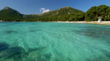 Mallorca, İspanya'da güzel deniz ve plaj. Parlak güneşli bir gün boyunca rüzgarda sallanan Akdeniz'in şeffaf turkuaz suyunu temizleyin. 4k