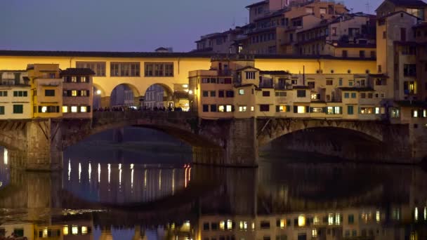 Флоренції, Італія. Панорама мосту Понте Веккіо увечері. Нічні ліхтарі відображені в водах річки Арно. Готель "Флоренція" розташований в регіоні Тоскана. Панорамування, 4K — стокове відео