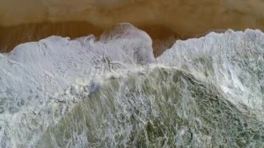 Portekiz. Atlantik okyanusunun köpüklü yeşil dalgalarının kumlu plaja yuvarlanan yukarıdan aşağıya doğru çekilmiş havadan çekilmiş fotoğrafı. Uhd