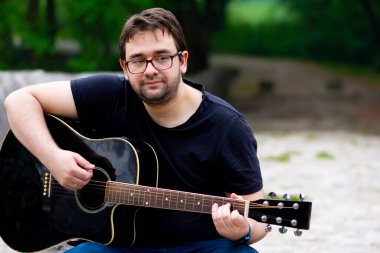 Gözlüklü genç adam eski Roma köprüsünde oturmuş gitar çalıyor.