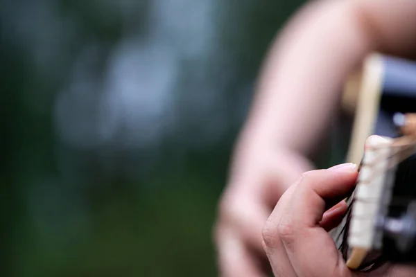 Açık havada akustik gitar çalan bir kızın yakın plan fotoğrafı..