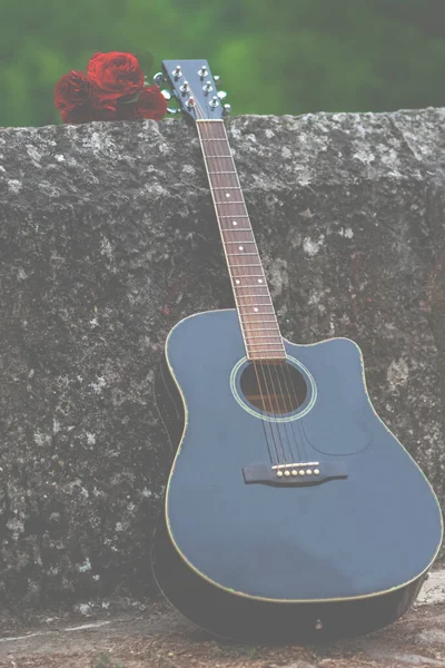 Acoustic guitar and bouquet of red roses on the old bridge wall. Romantic and beautiful scene in nature