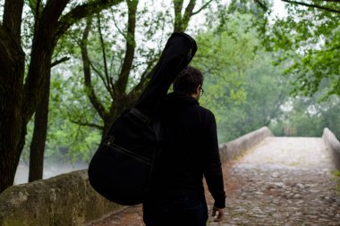 Genç adam ormanda tek başına yürürken gitar çantası taşıyor. Doğanın tadını çıkarıyorum güzellik