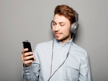 Kulaklık takan ve cep telefonu tutan genç bir adam. 