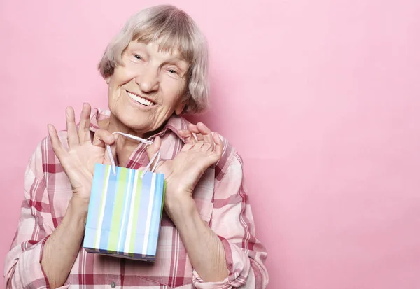 Estilo de vida y el concepto de la gente: Mujer mayor feliz con bolsa de compras sobre fondo rosa — Foto de Stock