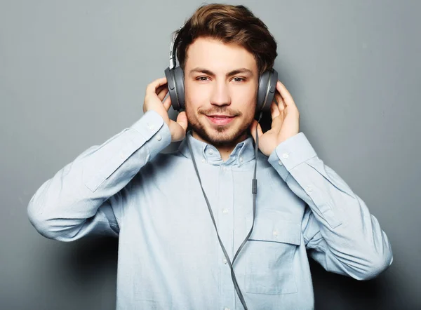 Estilo de vida, felicidad, concepto emocional y de personas: Disfrutando de su música favorita. Feliz joven elegante hombre ajustando sus auriculares anuncio sonriendo — Foto de Stock