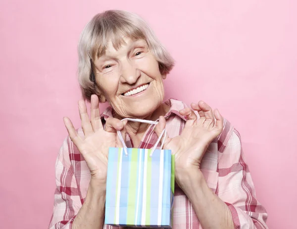 Estilo de vida y el concepto de la gente: Mujer mayor feliz con bolsa de compras sobre fondo rosa —  Fotos de Stock