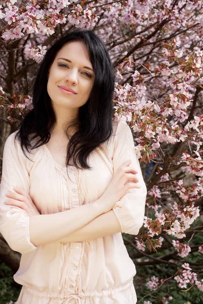 Retrato de uma bela jovem mulher em um fundo de flores de cereja rosa na primavera , — Fotografia de Stock