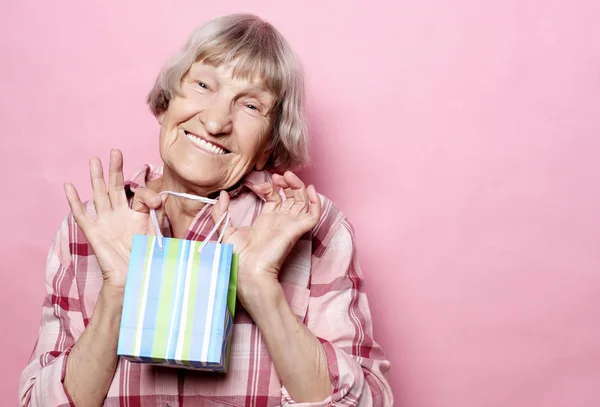 Estilo de vida y el concepto de la gente: Mujer mayor feliz con bolsa de compras sobre fondo rosa — Foto de Stock