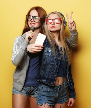 Mikrofonlu iki kız şarkı söyleyip birlikte eğleniyorlar, selfie çekiyorlar.