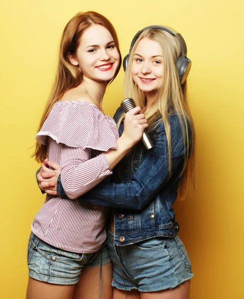 Twee jonge meisjes zingen over gele achtergrond — Stockfoto