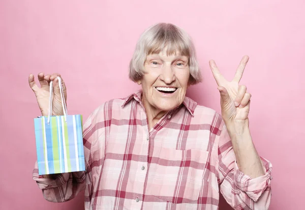 Estilo de vida y el concepto de la gente: Mujer mayor feliz con bolsa de compras sobre fondo rosa — Foto de Stock