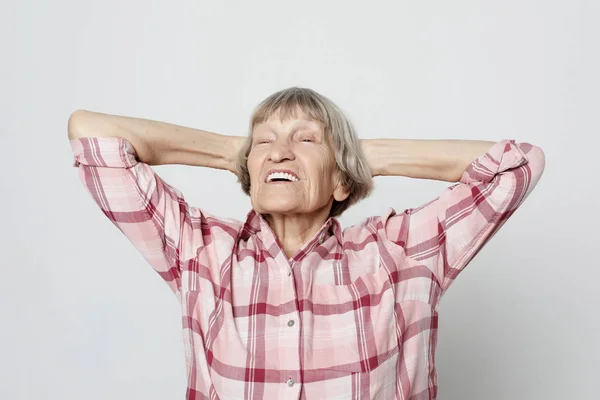 Feliz abuela en una camisa rosa cruzó sus brazos sobre su cabeza — Foto de Stock