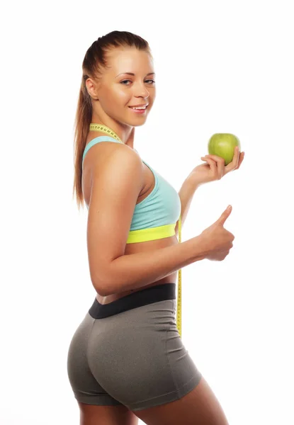 Sport, dieta, zdrowie i koncepcja ludzi: Młoda pogodna kobieta w stroju sportowym z jabłkiem, odizolowana na białym tle — Zdjęcie stockowe
