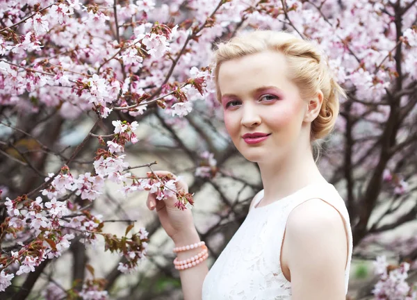 Retrato de una hermosa joven rubia sobre un fondo de flores de cerezo rosadas en primavera —  Fotos de Stock