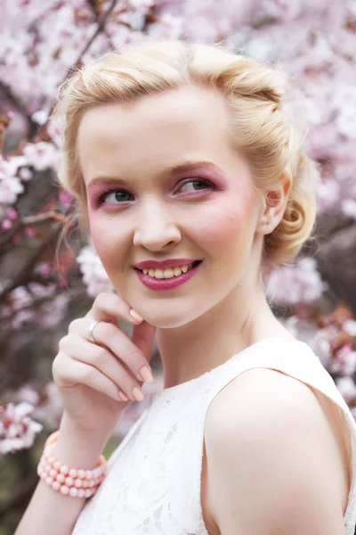 Retrato de una hermosa joven rubia sobre un fondo de flores de cerezo rosadas en primavera —  Fotos de Stock