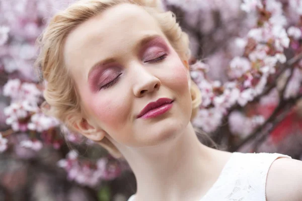 Egy gyönyörű, fiatal szőke nő portréja tavasszal rózsaszín cseresznyevirágok hátterében — Stock Fotó
