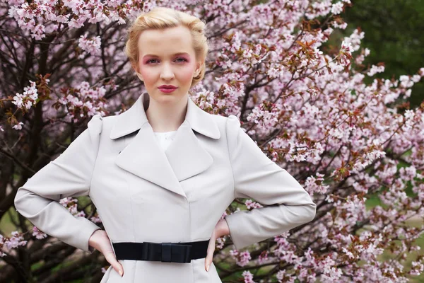 Retrato de una hermosa joven rubia sobre un fondo de flores de cerezo rosadas en primavera — Foto de Stock