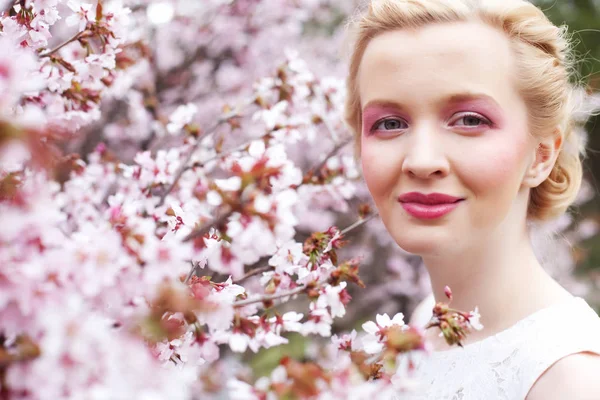 Retrato de uma bela jovem loira em um fundo de flores de cereja rosa na primavera — Fotografia de Stock