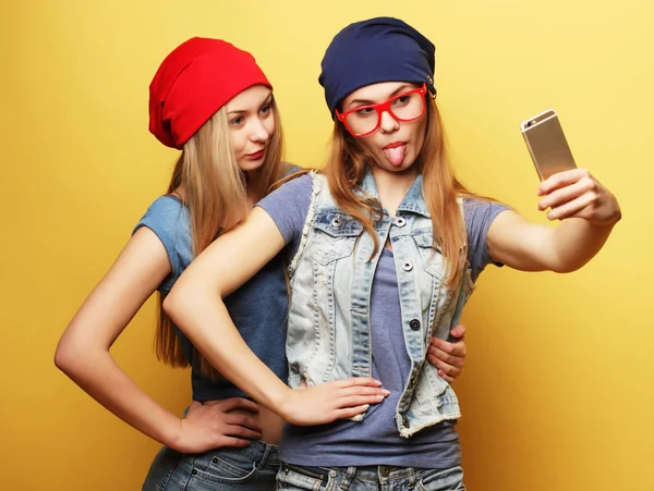 Due giovani ragazze hipster amici prendendo selfie su sfondo giallo — Foto Stock