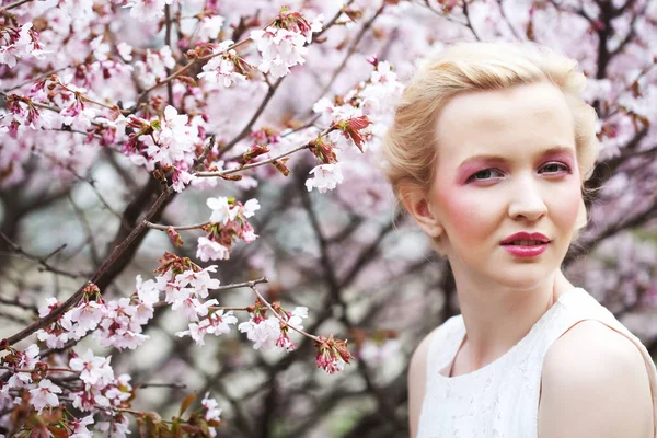 Retrato de una hermosa joven rubia sobre un fondo de flores de cerezo rosadas en primavera —  Fotos de Stock