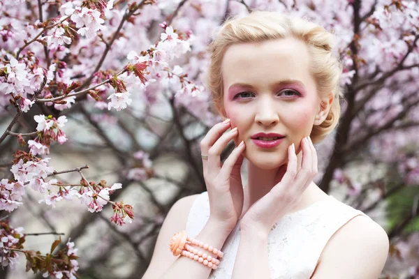 Porträtt av en vacker ung blond kvinna på en bakgrund av rosa körsbär blommor på våren — Stockfoto