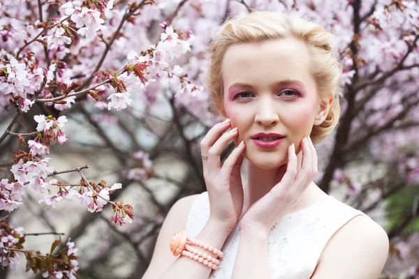 Retrato de una hermosa joven rubia sobre un fondo de flores de cerezo rosadas en primavera — Foto de Stock