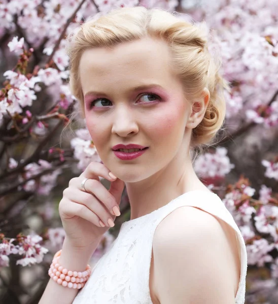 Retrato de una hermosa joven rubia sobre un fondo de flores de cerezo rosadas en primavera —  Fotos de Stock