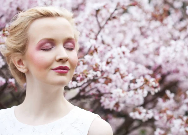 Retrato de uma bela jovem loira em um fundo de flores de cereja rosa na primavera — Fotografia de Stock