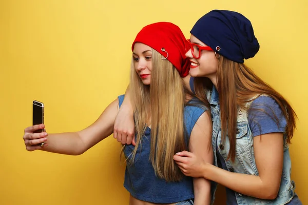 Due giovani ragazze hipster amici prendendo selfie su sfondo giallo — Foto Stock