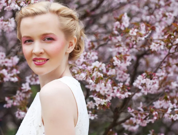 Porträt einer schönen jungen blonden Frau vor rosa Kirschblüten im Frühling — Stockfoto