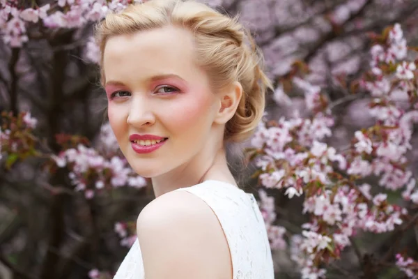 Retrato de una hermosa joven rubia sobre un fondo de flores de cerezo rosadas en primavera — Foto de Stock