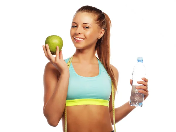 Cheerful woman in sports wear with apple and a bottle of water, isolated over white background — Stock Photo, Image