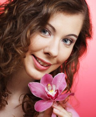 Pembe arka planda orkide çiçeğiyle güzel mutlu bir kadın.